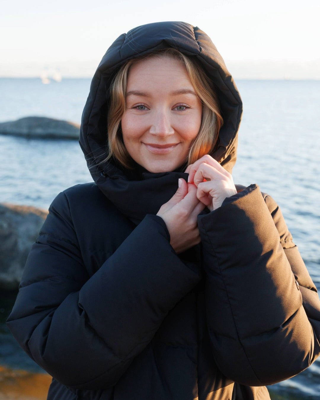 Woman wearing a black hooded coat by a body of water