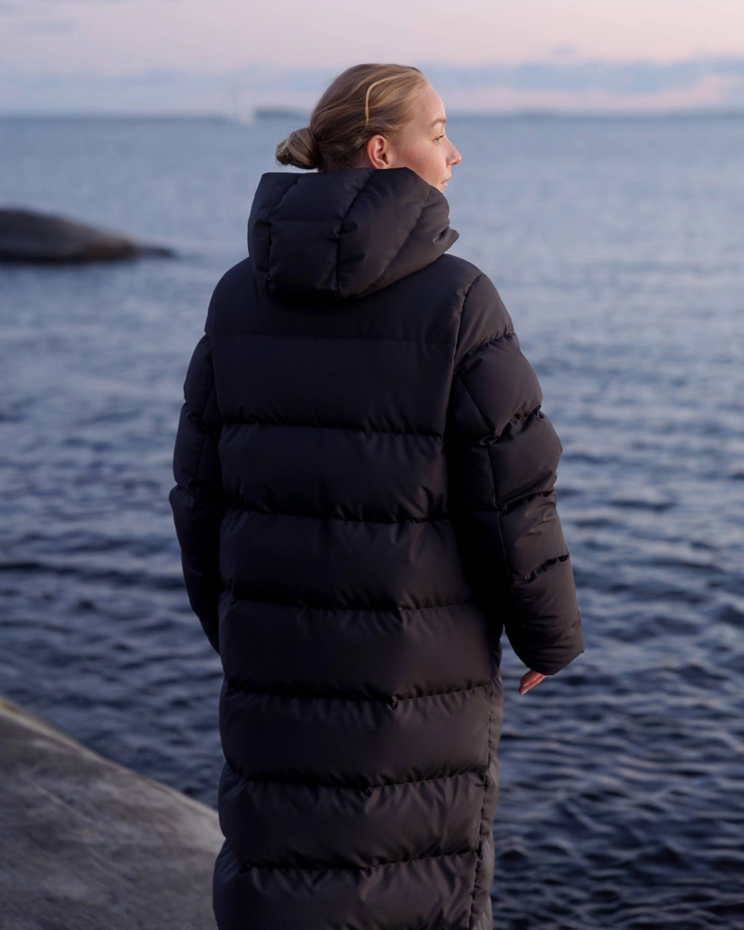Person wearing a black down coat standing by a body of water