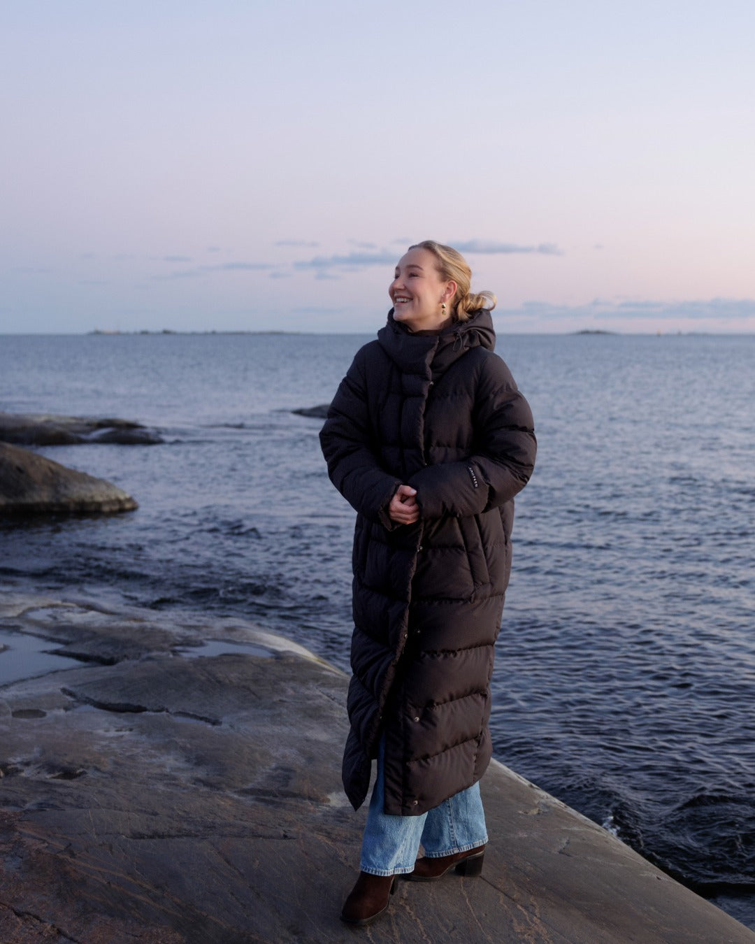 Person wearing a long dark coat standing by the water
