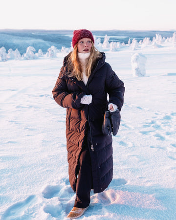 Person wearing a long black (color: Black bird) down coat in a snowy landscape