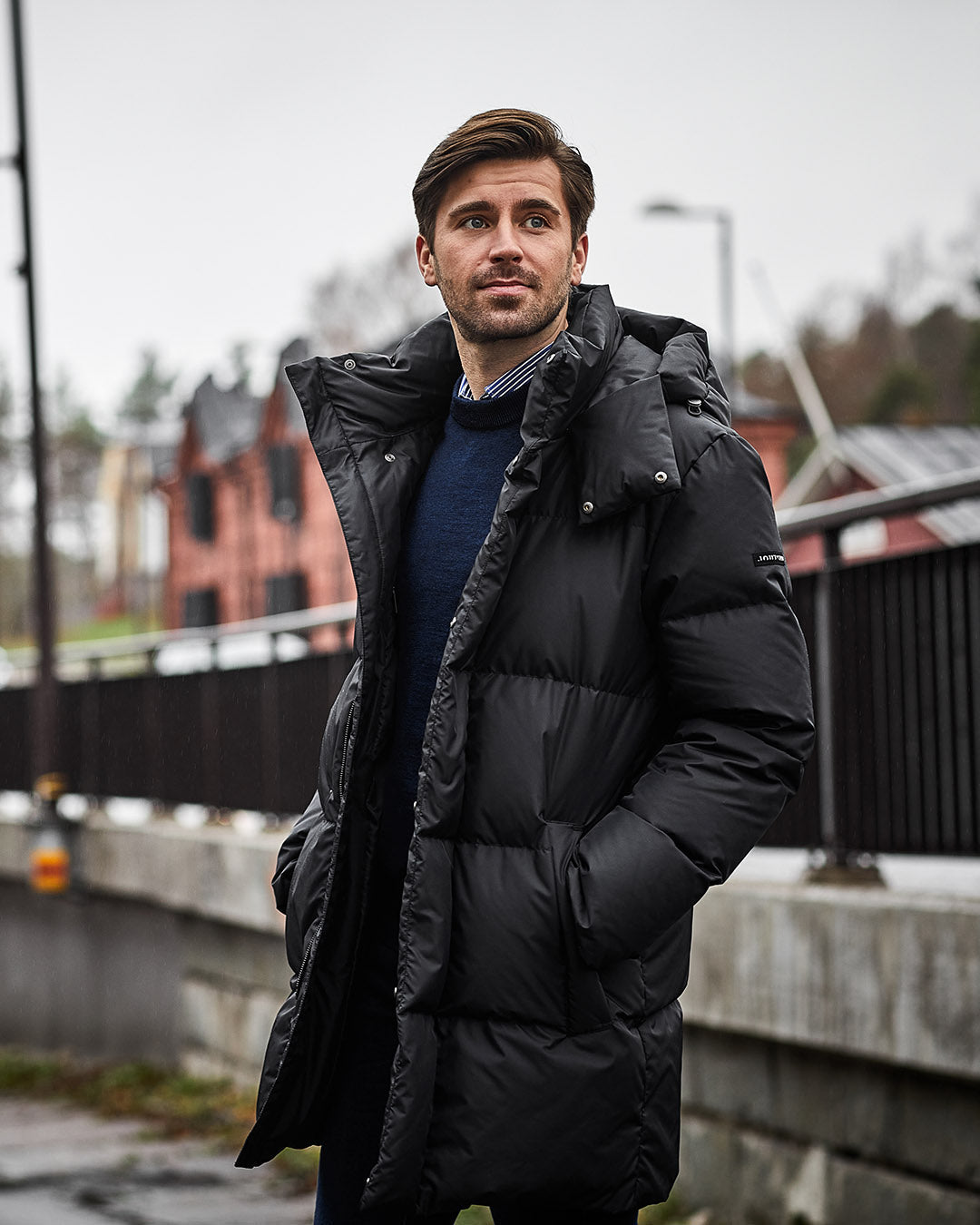 Man wearing a black down coat standing outdoors on a cloudy day.