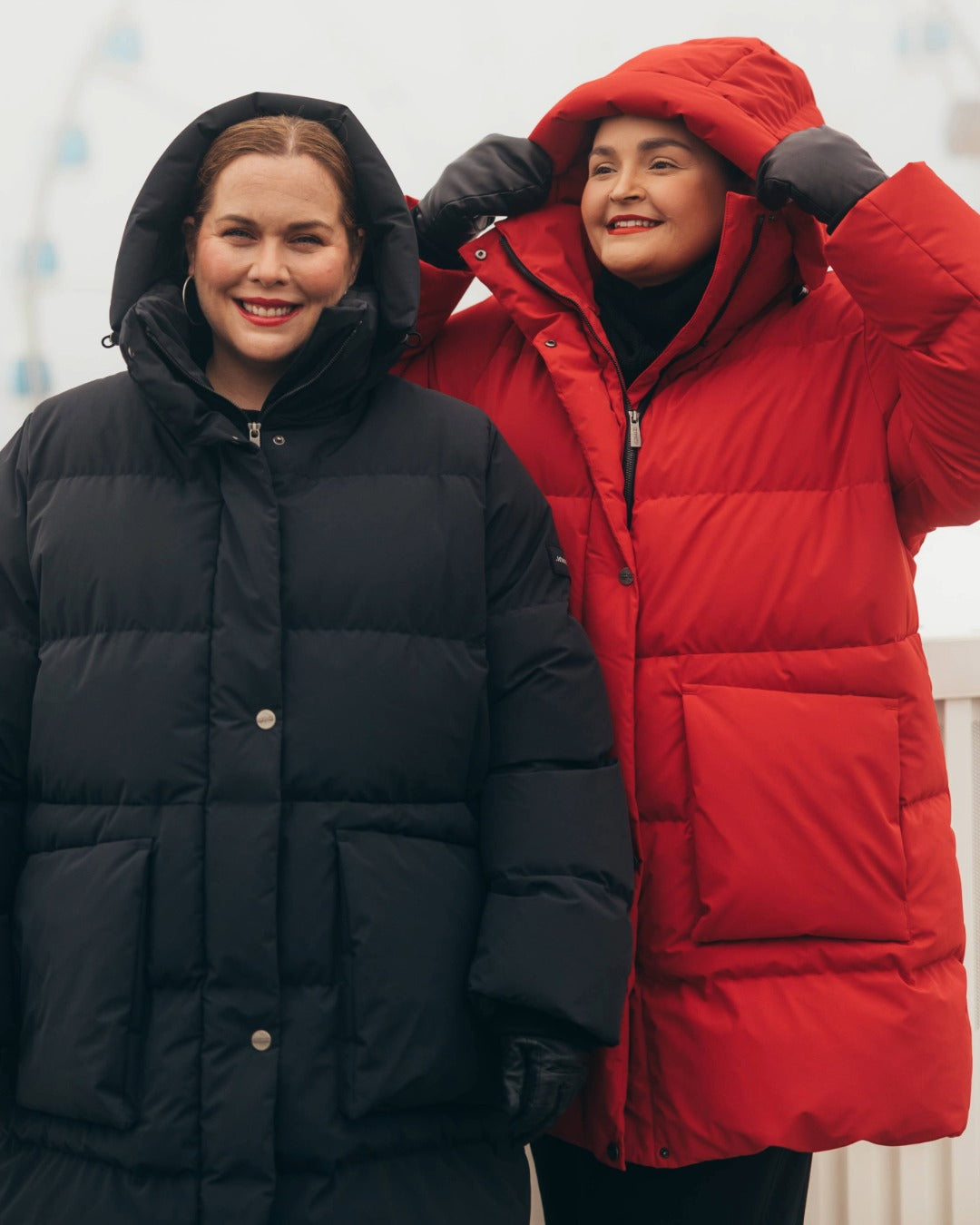 Two people wearing down jackets, one black and one red, standing close together.