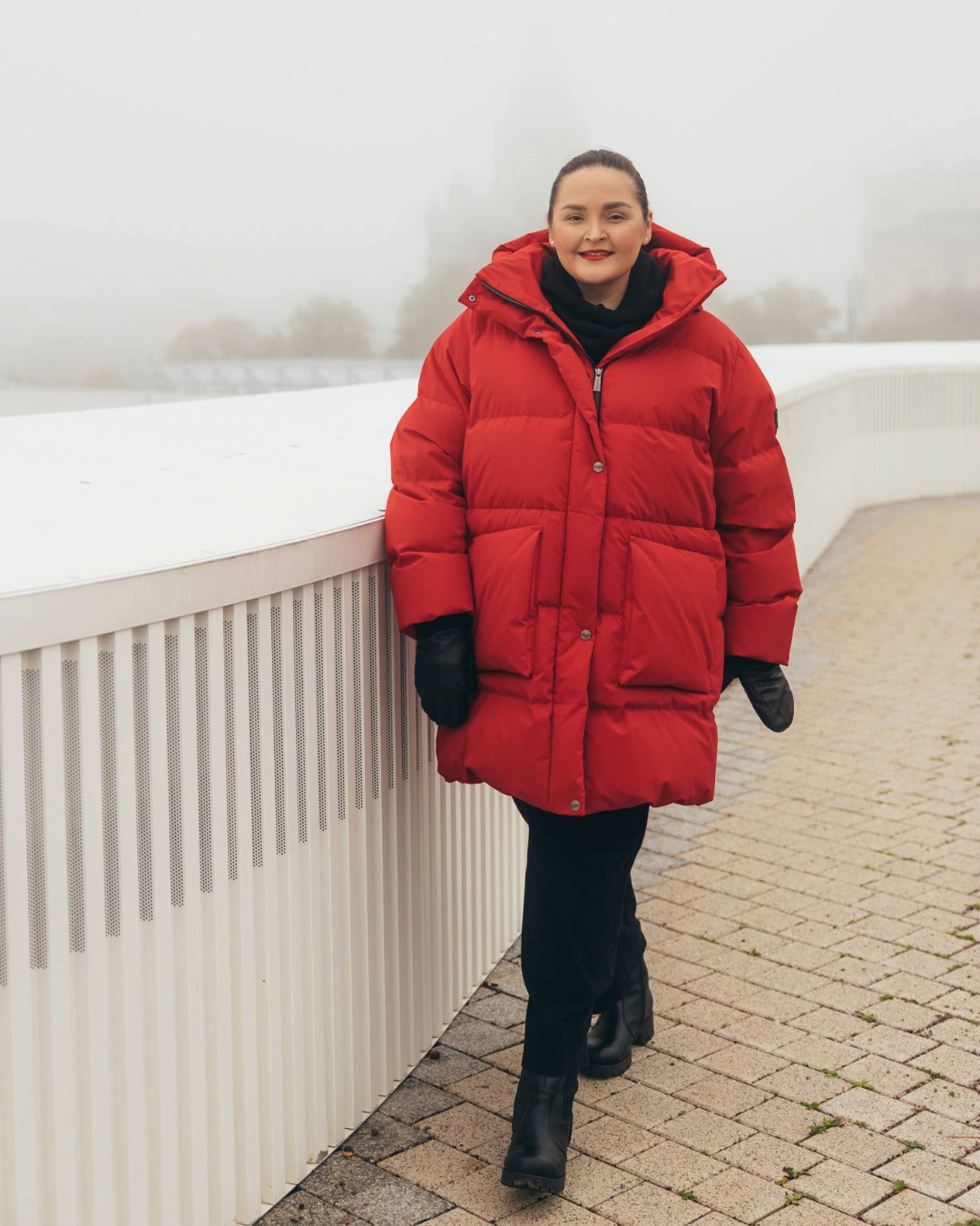 Person wearing a red down coat standing on a sidewalk.