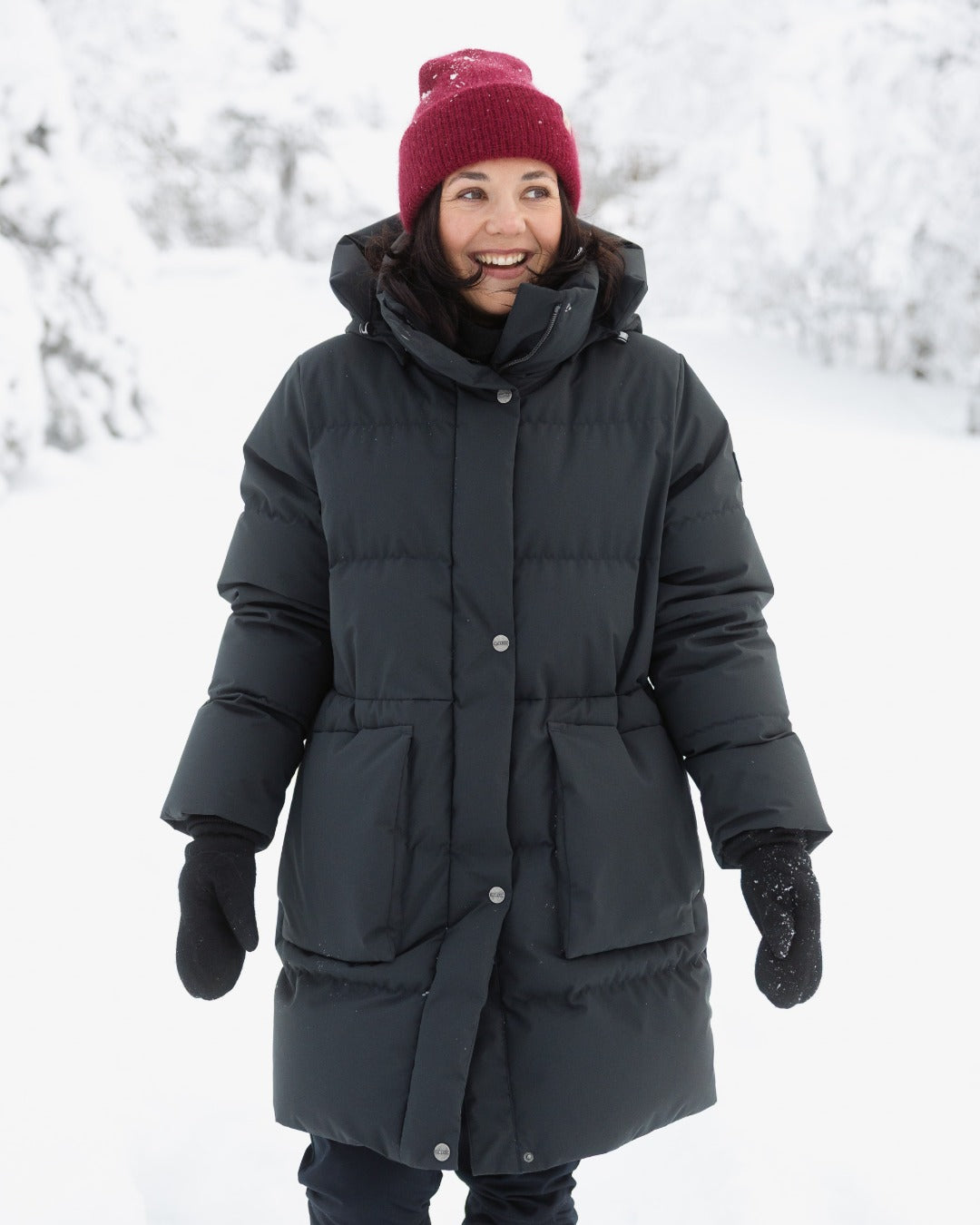 Person wearing a black (color: Jet black) down coat and red beanie standing in a snowy landscape