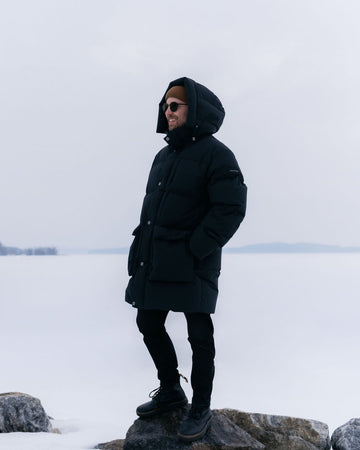 Person wearing a black Tuisku down coat standing on a snowy landscape