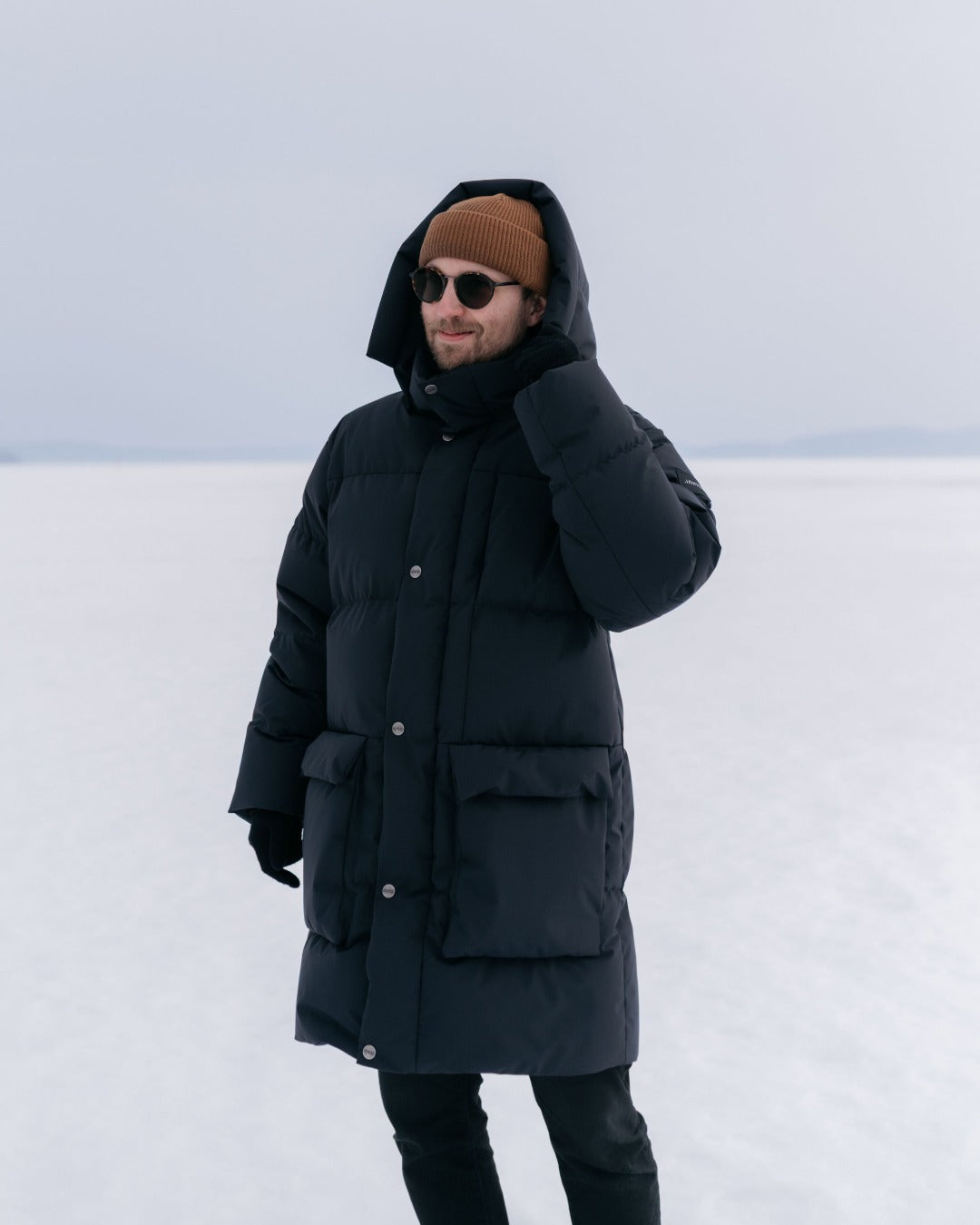 Person wearing a black Tuisku down coat and brown beanie in a snowy landscape