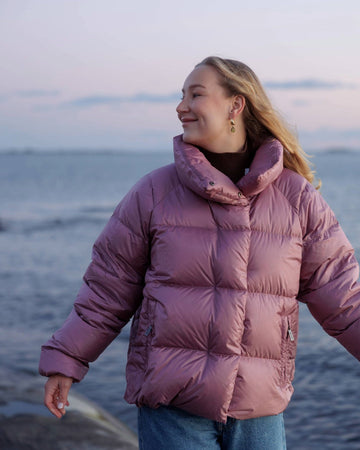 Person wearing a pink down coat standing by the ocean