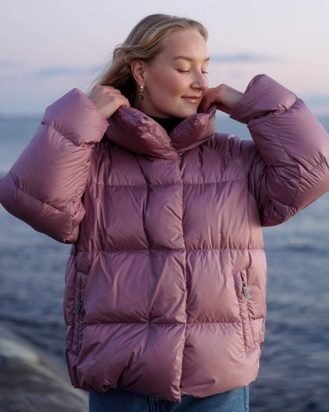 Person wearing a pink down coat by the water.