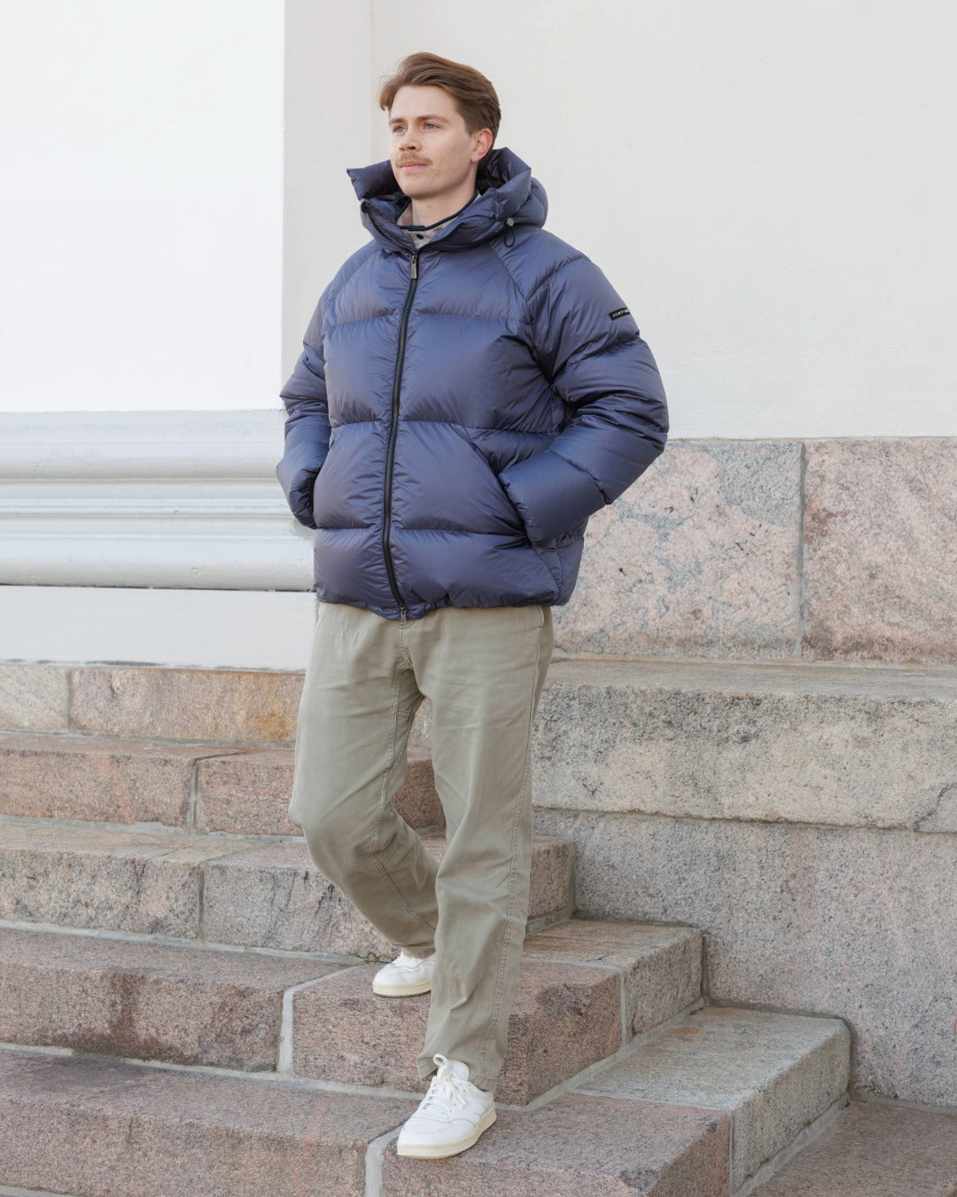 Man wearing a blue Huurre down coat standing on stone steps.