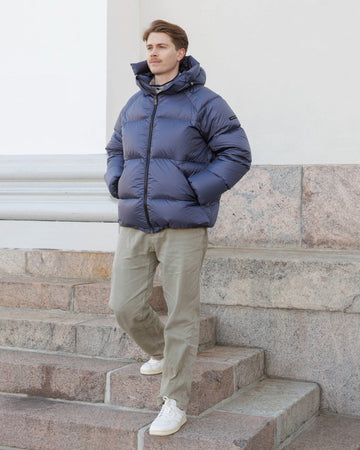 Man wearing a blue Huurre down coat standing on stone steps.