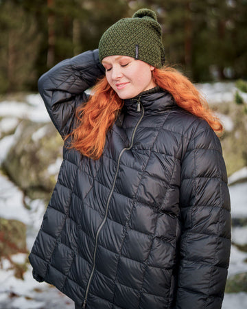 Woman wearing a charcoal black Tulppaani light down coat with square quilting and a stand-up collar. The coat has a front zipper closure and a relaxed, slightly flared fit.