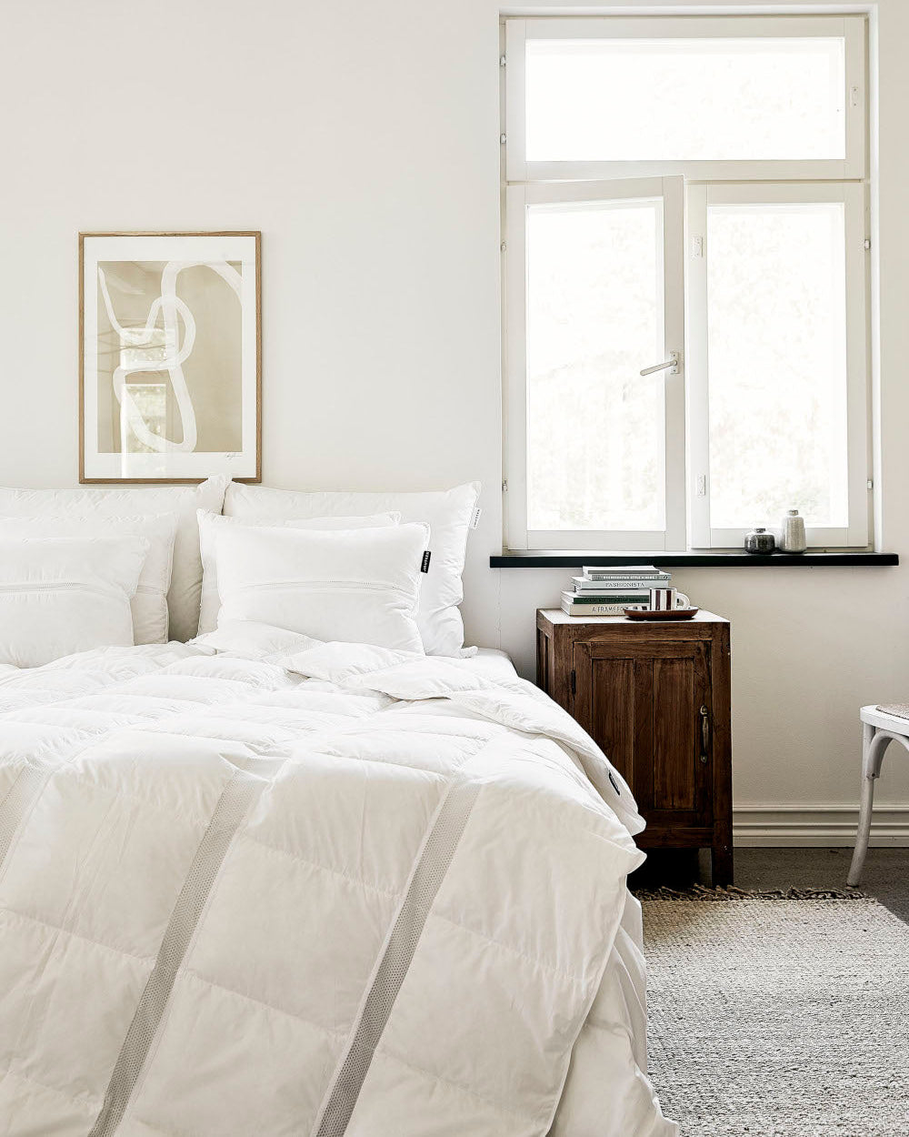 Neatly made bed in a bedroom with a window and side table.