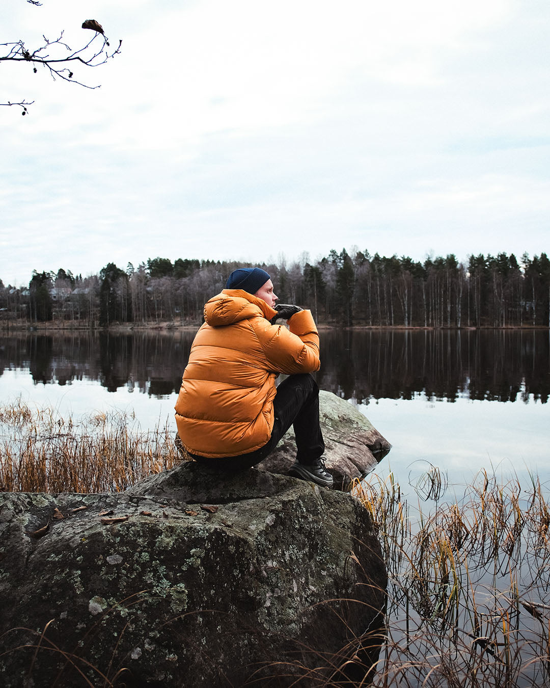 Person sitting on a rock by a lake wearing an orange down coat