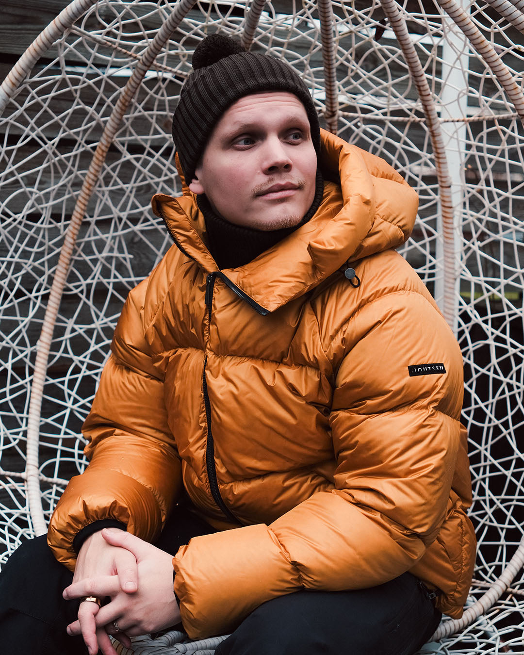 Person wearing an orange down coat sitting in a decorative chair.
