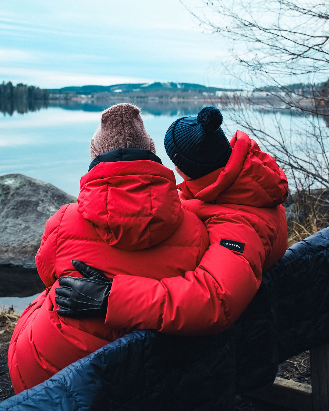 Two people in red down coats sitting by a lake on a cold day.