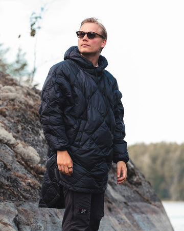 Person wearing a black Velho down anorak standing on rocky terrain with a natural background