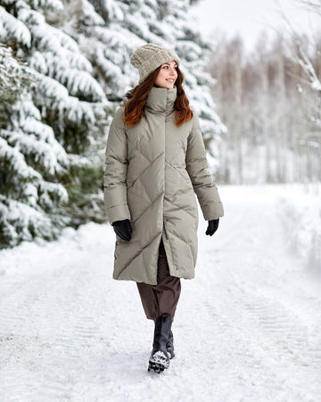 Woman in a long beige coat walking in a snowy forest