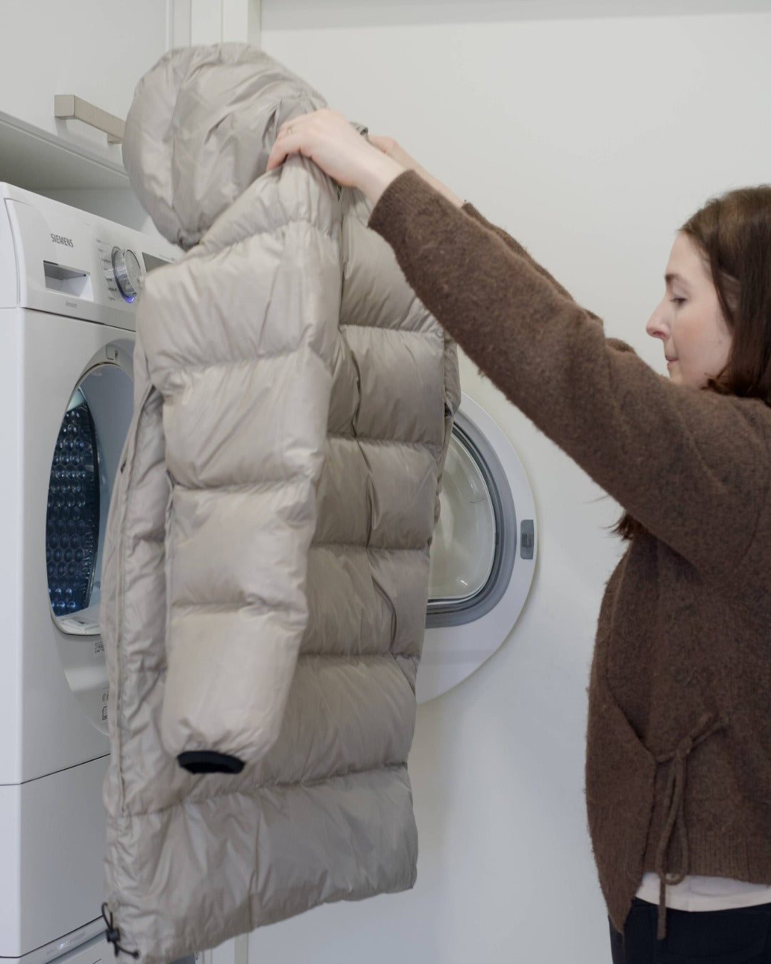 A woman holding a light down coat after drying machine