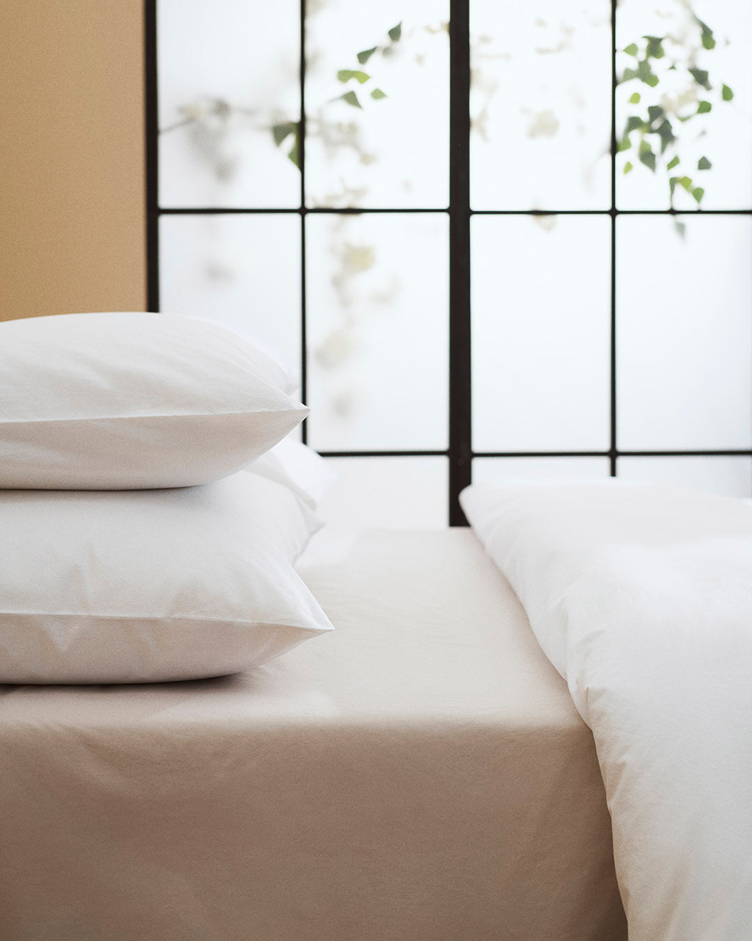Stack of white pillows on a bed with a window in the background