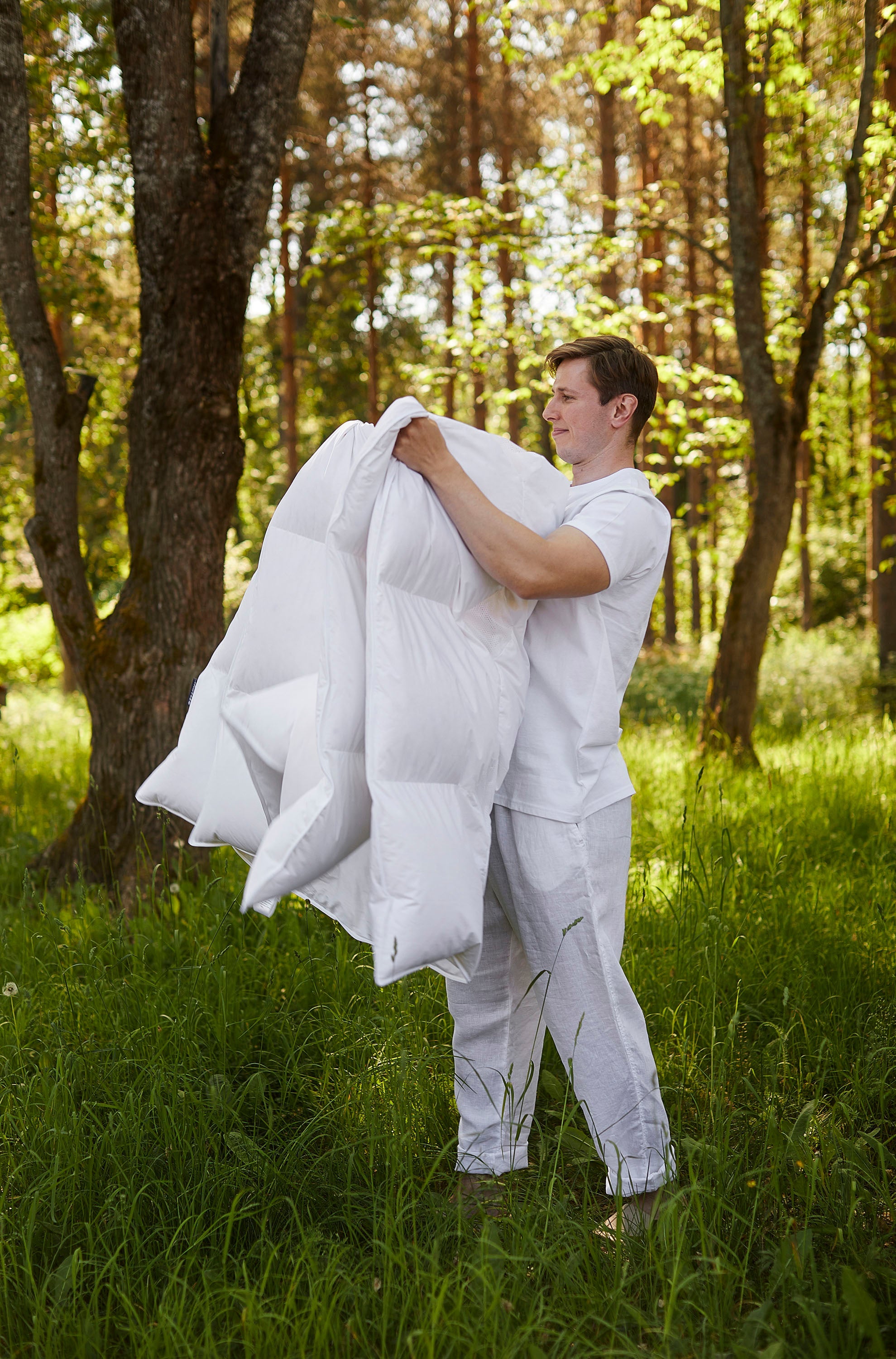 Person holding a large white down blanket in a forest setting