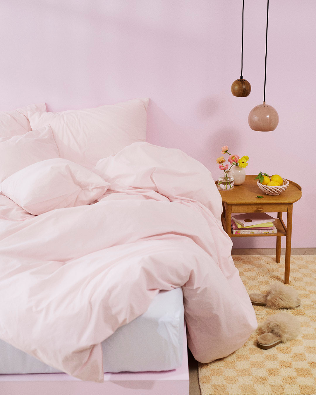 Pink comforter on a bed in a room with a side table and decor items.
