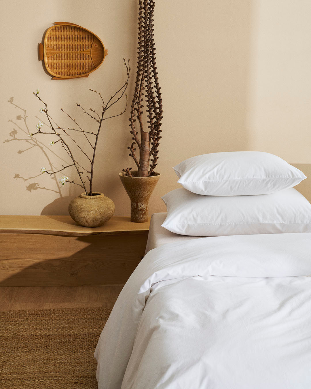 Bedroom with white bedding, wooden nightstand, and decorative plants.