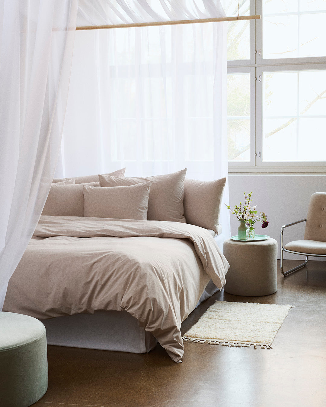 Neatly made bed with beige bedding in a bright bedroom.