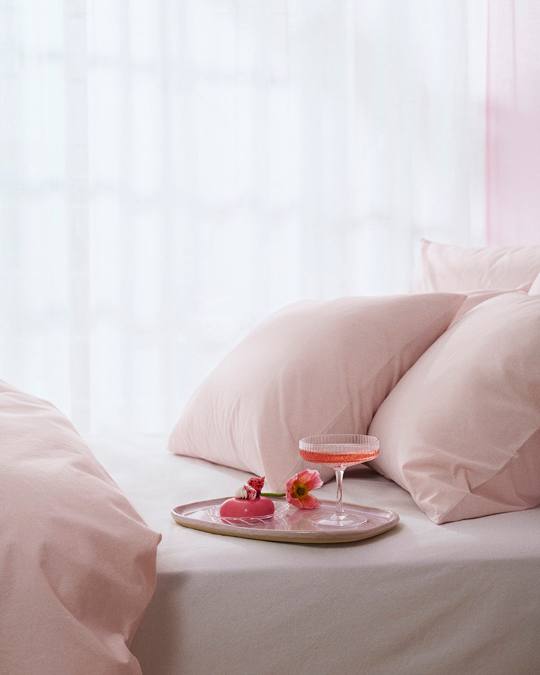 Tray with a glass and two small pink flamingo figurines on a bed with beige bedding.