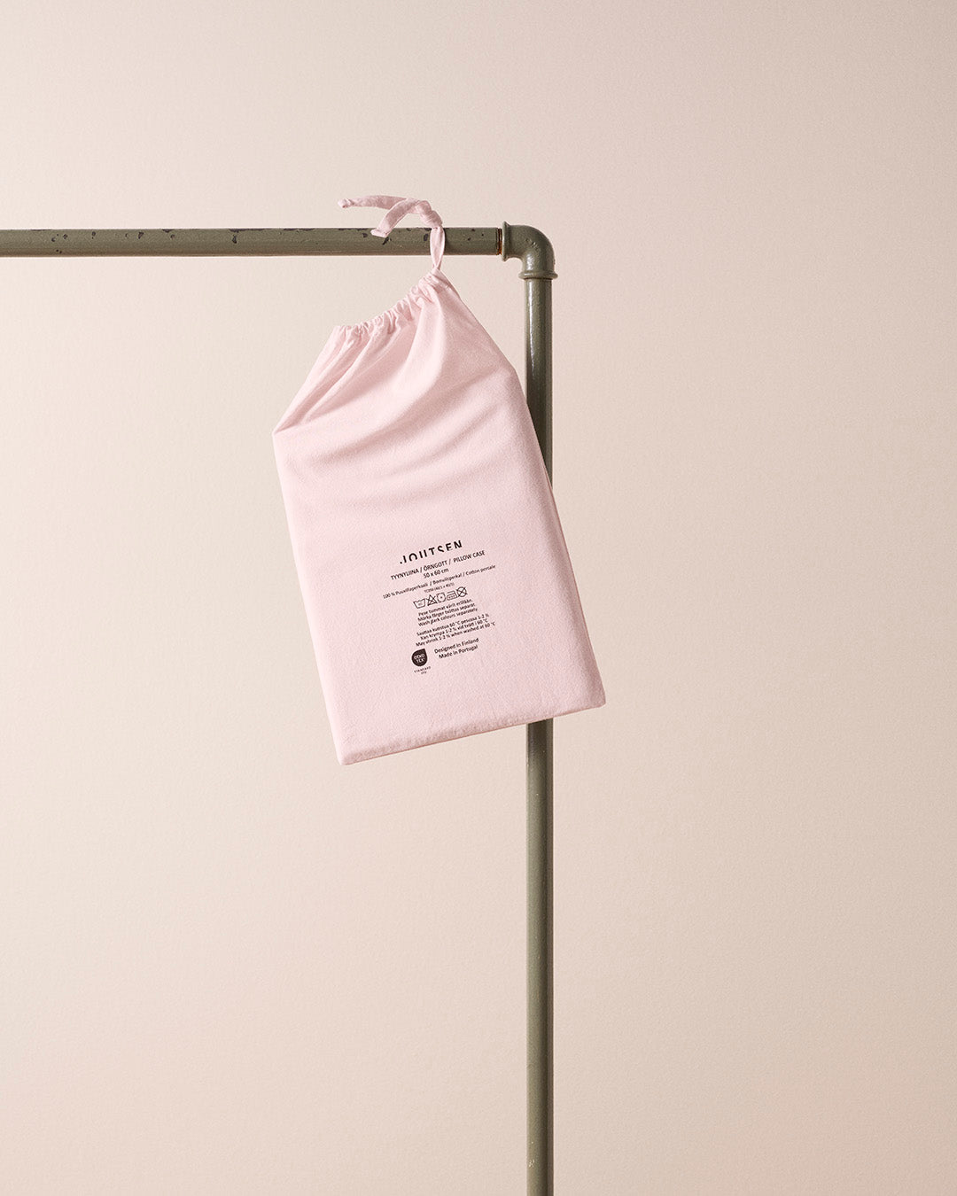 Pink drawstring bag with text on a metal rack against a light beige background