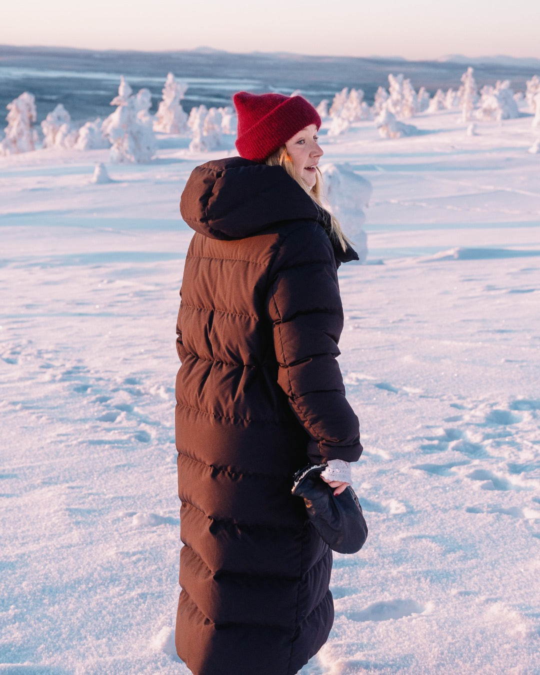 Person wearing a black (color: Black bird) down coat and red beanie standing in a snowy landscape with snow-covered trees.