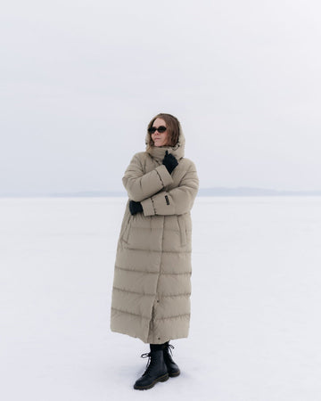 Person wearing a long beige Blenda down coat in a snowy landscape