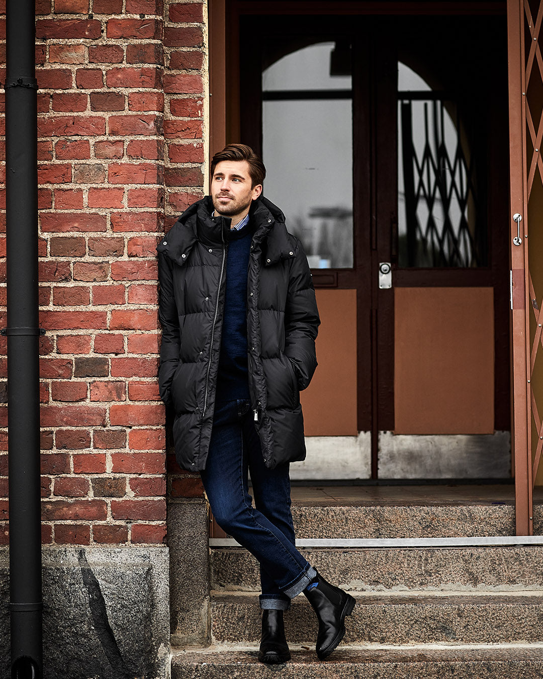 Man in a black coat leaning against a brick wall