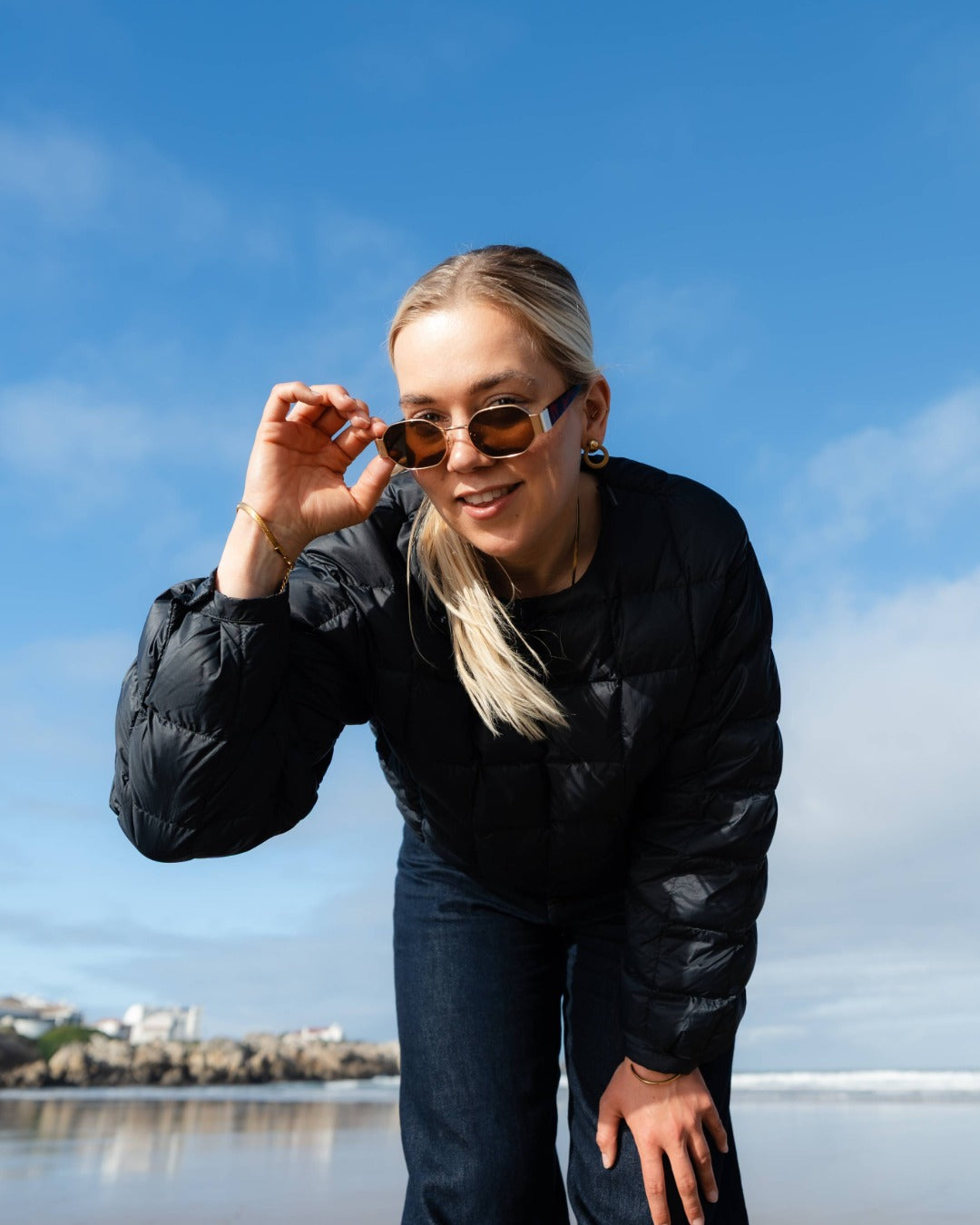 Woman wearing sunglasses and a black down shirt outdoors with a blue sky background