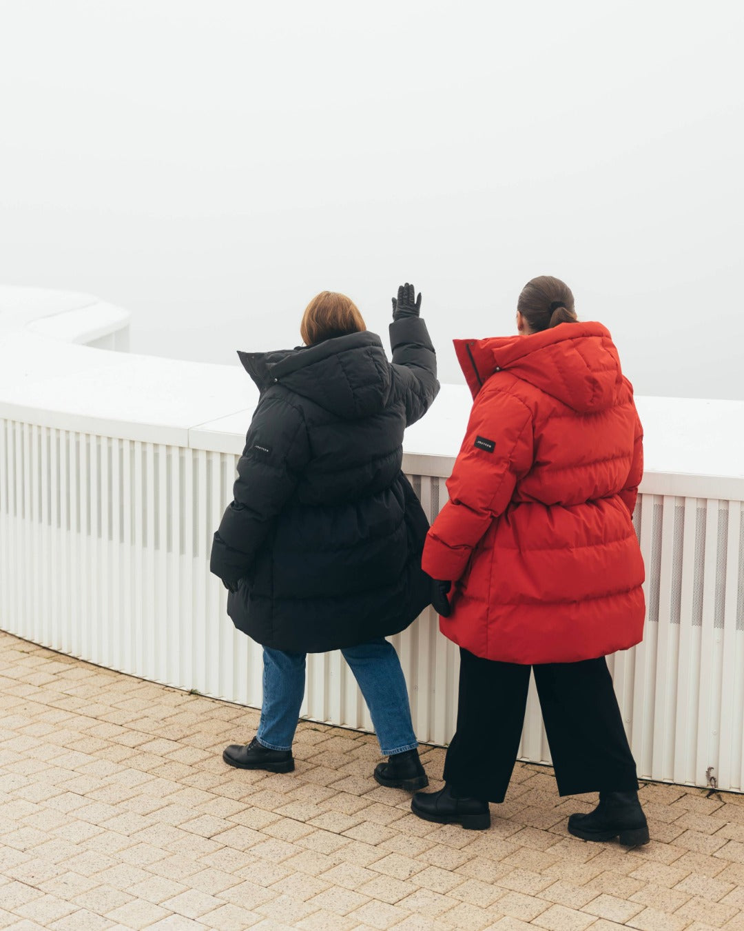 Two people wearing down jackets, one black and one red, standing on a sidewalk.