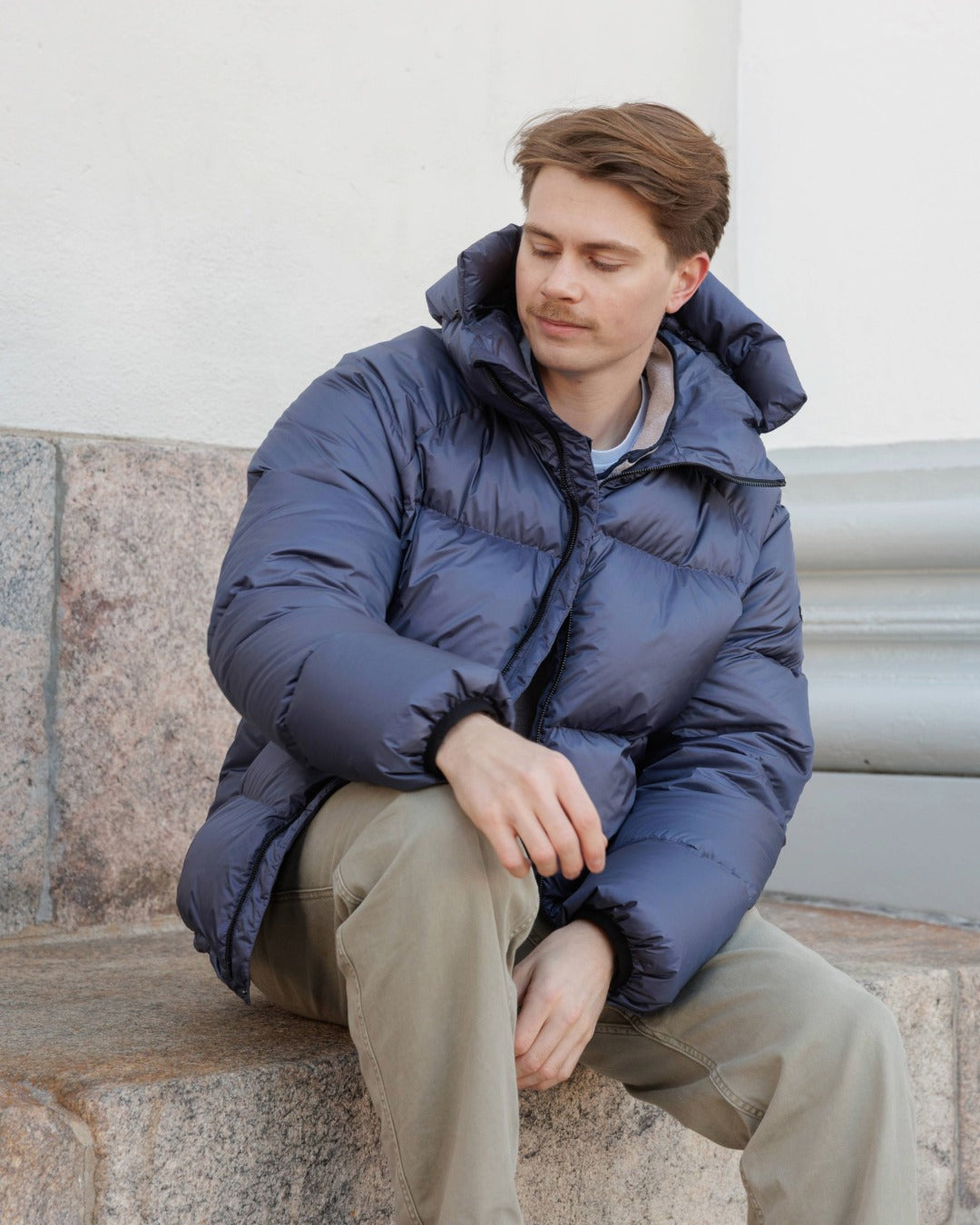 Man wearing a blue Huurre down coat sitting on stone steps.
