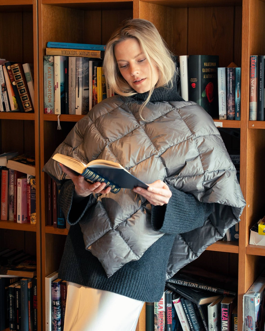 Woman reading a book in a library setting wearing a light Unelma down poncho