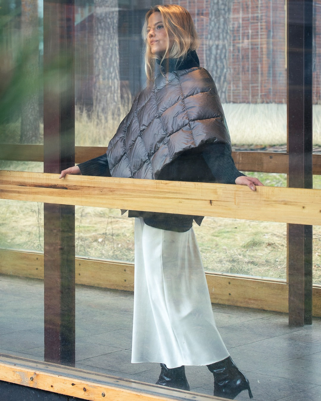 Woman wearing alight Unelma down poncho and white dress standing by a wooden railing.