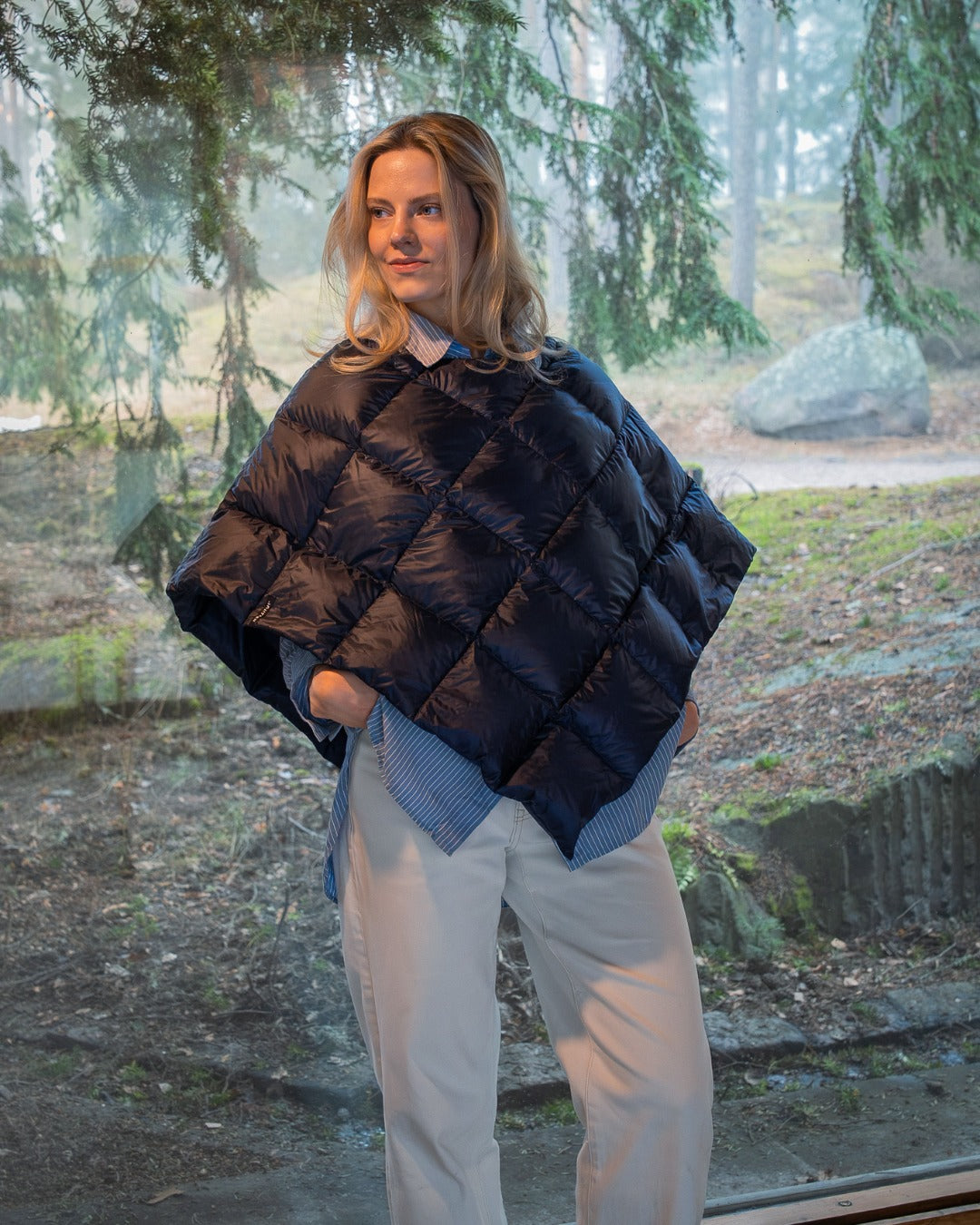 Person wearing a dark blue Unelma down poncho in a forest setting