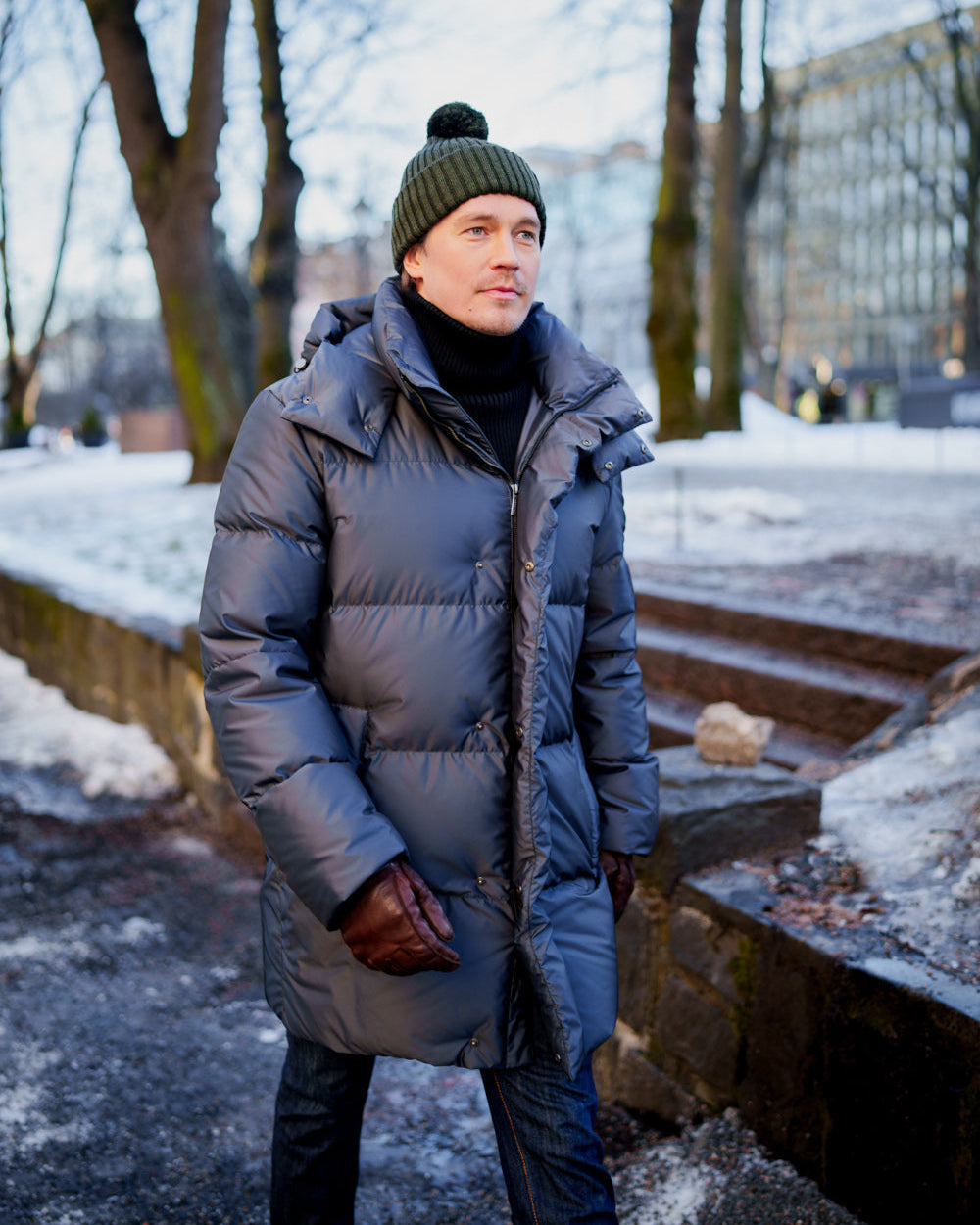 Man wearing a long down coat and green beanie standing outdoors in winter.
