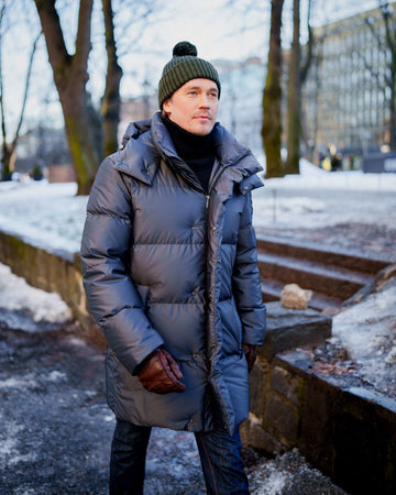 Man wearing a long down coat and green beanie standing outdoors in winter.