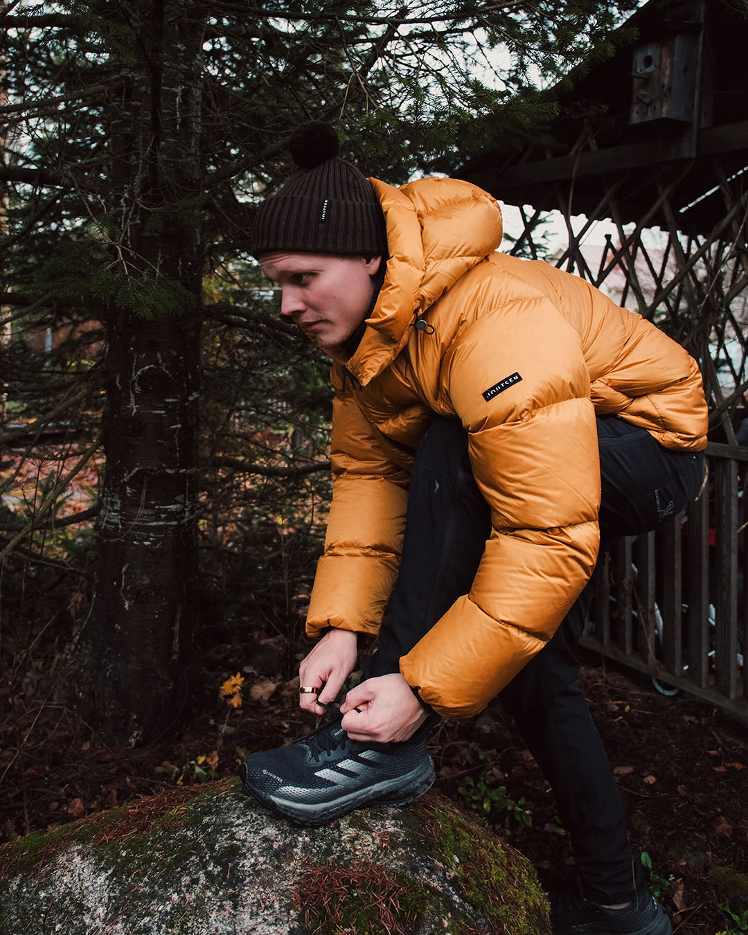 Person in orange down coat and black pants tying shoes outdoors