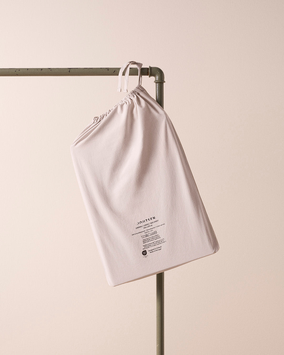 Light gray drawstring bag hanging on a metal rack against a beige background
