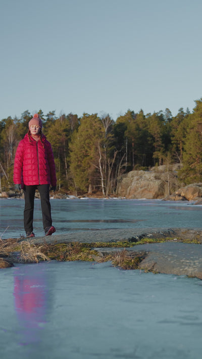 A woman wearing red light down coat is walking by the water