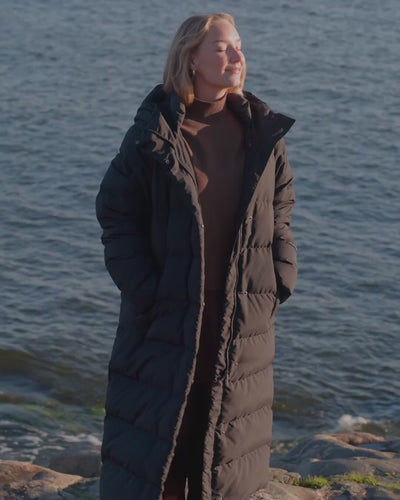 A woman is wearing a long down coat by the water