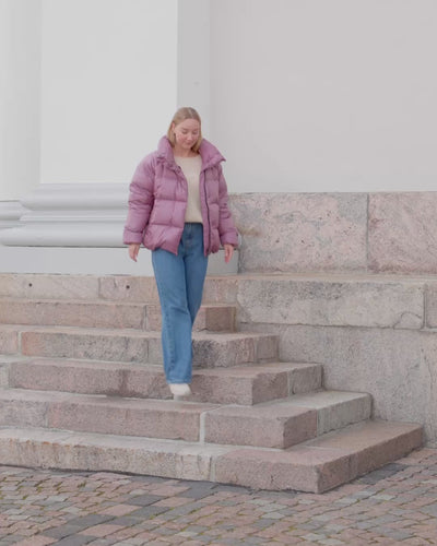 A woman is walking down the stairs and pulling up the zipper of her short down coat.