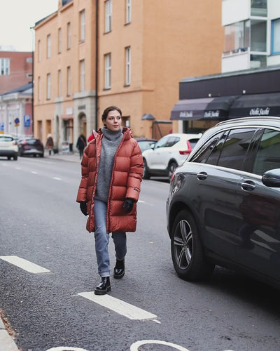 A woman strolling in the city wearing an orange down coat.