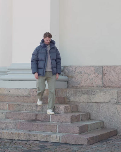 A man is walking stairs outside and putting on the zipper on his short down coat. 