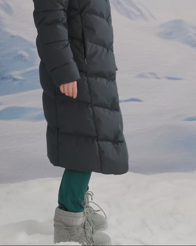A woman is wearing a long down coat in a snowy scene.