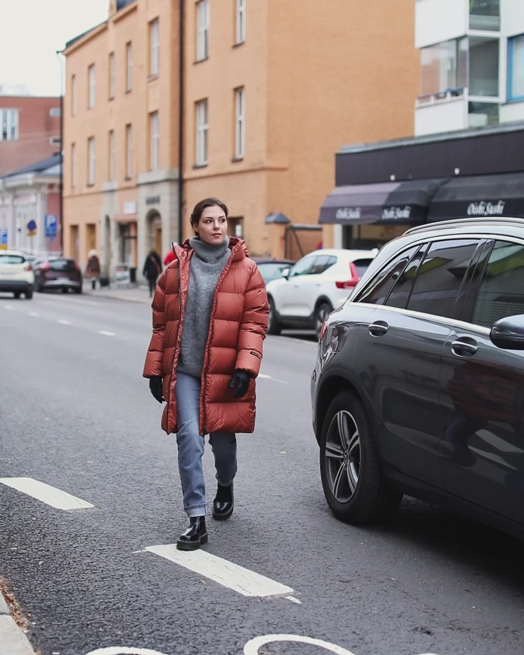 A woman strolling in the city wearing an orange down coat.