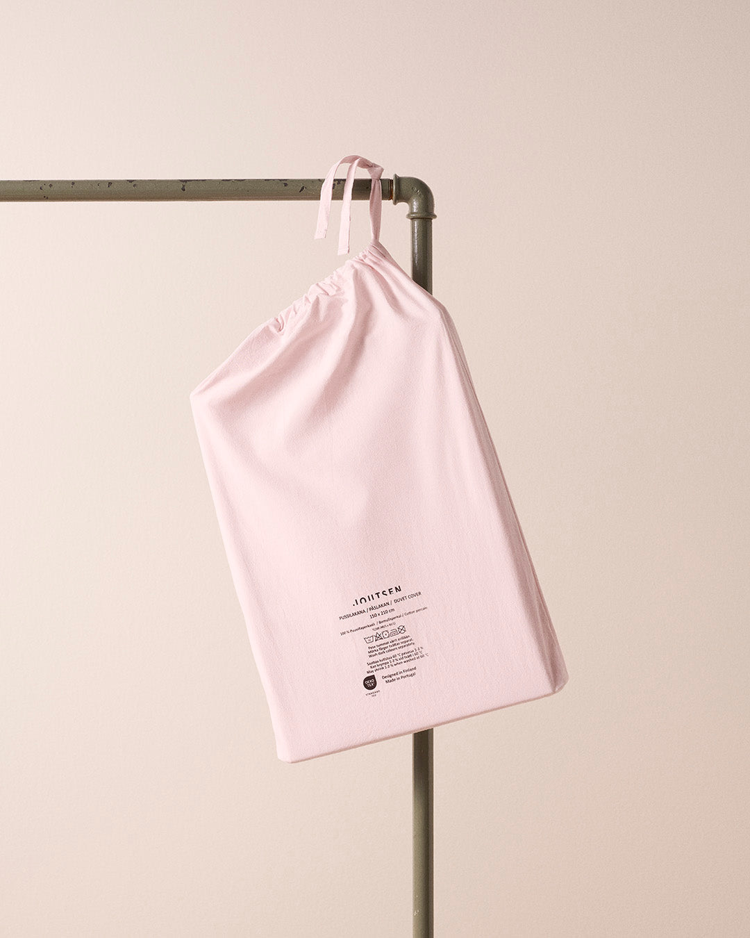 Pink drawstring bag with text on a metal rack against a beige background